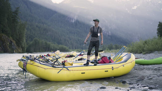 Hombre mirando hacia otro lado mientras está de pie en balsa en la orilla del río contra la montaña — Stock Photo