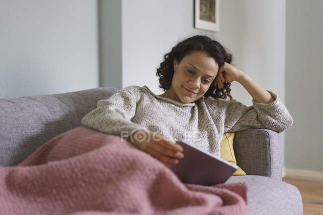 Lächelnde Frau mit digitalem Tablet beim Entspannen auf dem heimischen Sofa — Stockfoto