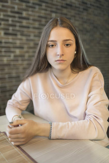Pensativo adolescente sentado a la mesa contra la pared de ladrillo - foto de stock