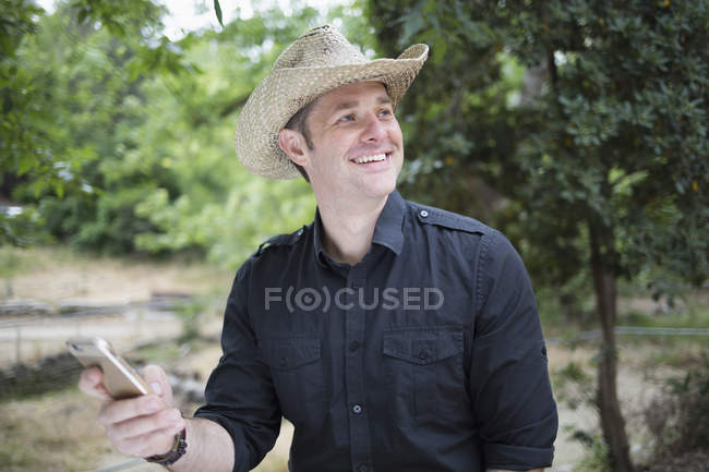 Счастливый мужчина отводит взгляд, держа смартфон в парке — стоковое фото