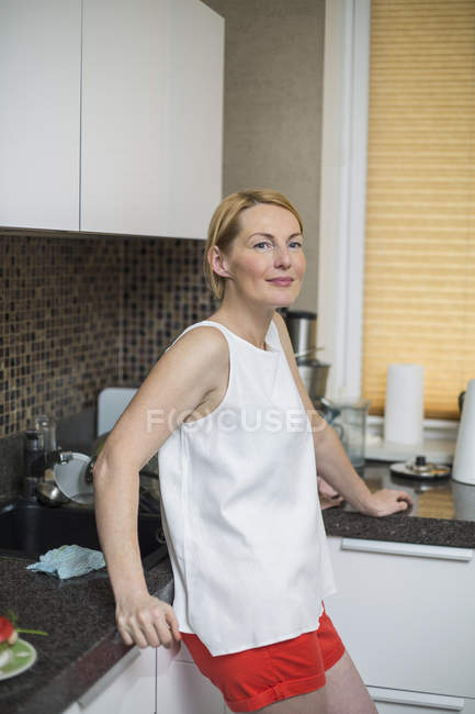 Smiling woman leaning at counter in kitchen — Stock Photo