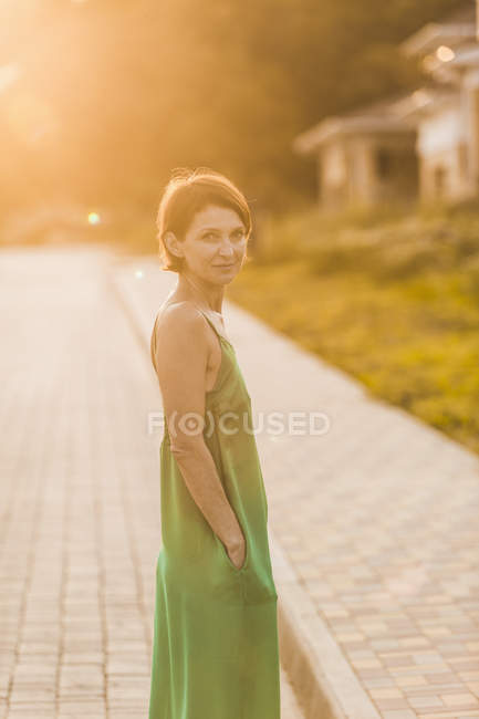 Portrait of woman standing on sidewalk at sunset against houses — Stock Photo