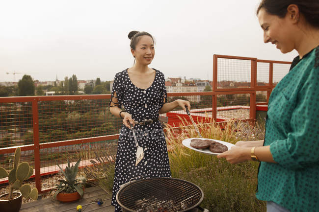 Smiling woman serving freshly grilled steak to female friend on patio — Stock Photo