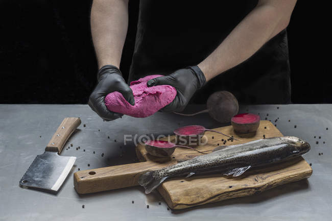 Milieu de l'homme pétrissant la pâte rose sur le poisson cru et les betteraves à table — Photo de stock