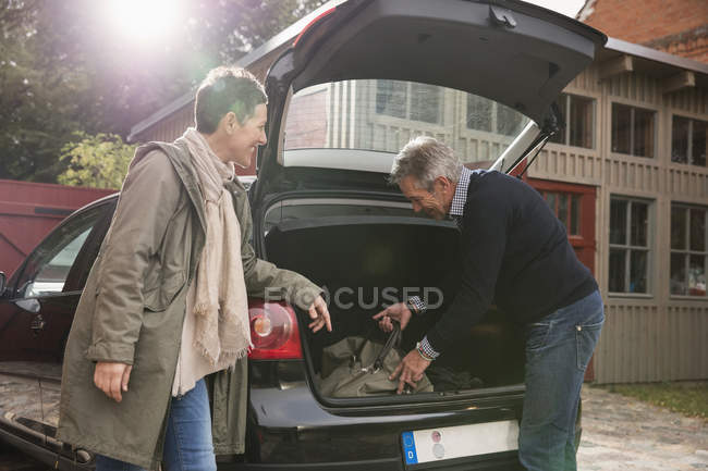 Woman watching man packing luggage in trunk — Stock Photo