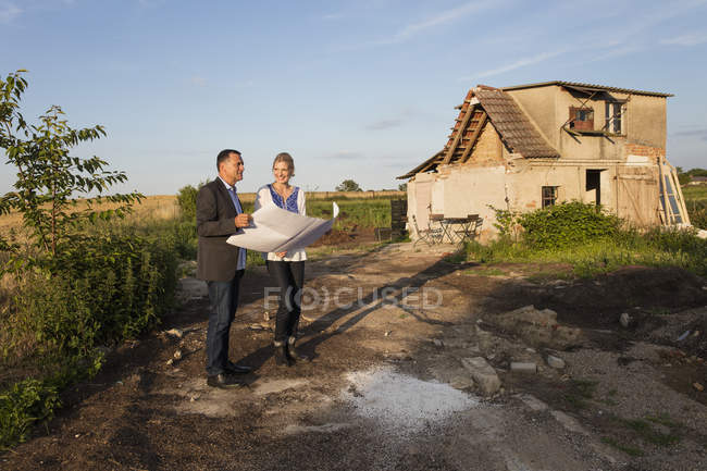 Mujer de pie con agente inmobiliario mientras lee documentos contra la casa en un día soleado - foto de stock