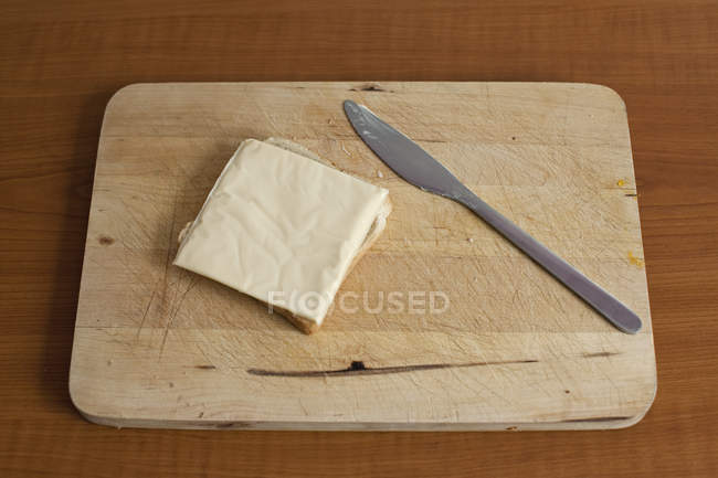 Slice of cheese on bread at wooden breadboard — Stock Photo