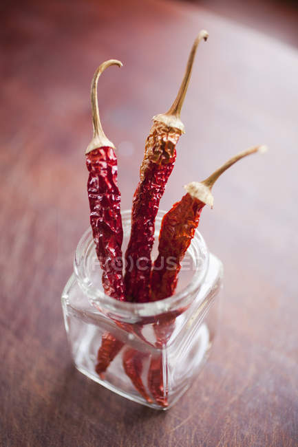Tre peperoncini secchi in vaso di vetro sul tavolo di legno — Foto stock