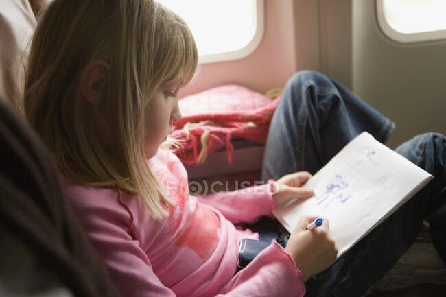 Chica joven sentada en un avión y dibujando en un bloc de bocetos - foto de stock