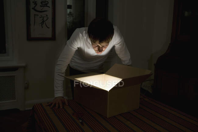 Jeune homme regardant dans une boîte en carton éclairée — Photo de stock