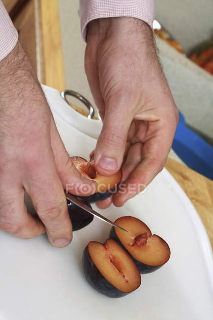 Crop male hands chopping plum fruit — Stock Photo