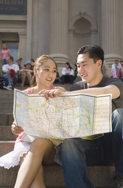 Young Chinese couple sitting on steps and holding map, New York City — Stock Photo