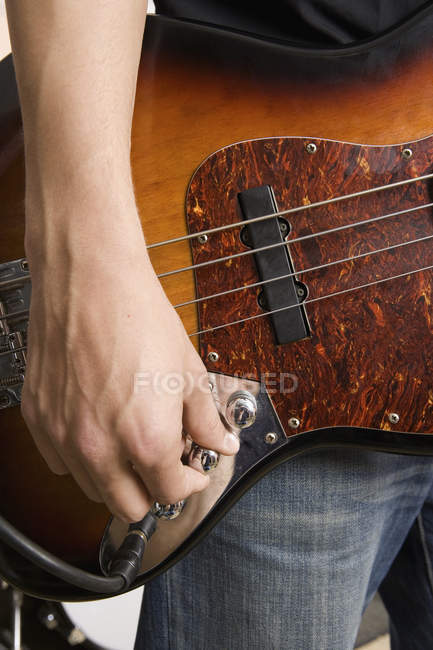 Mano del guitarrista Crop girando la perilla en la guitarra - foto de stock