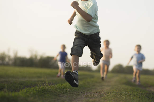Vista bassa di un ragazzo che corre in campo con altri bambini dietro — Foto stock