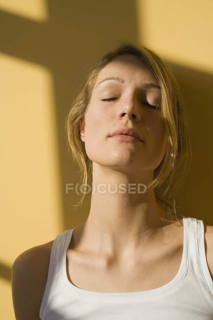Mujer joven de pie a la luz del sol con los ojos cerrados - foto de stock