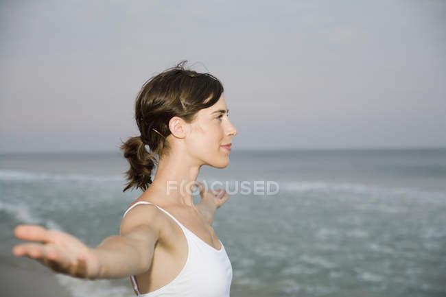 Donna in piedi sulla spiaggia con le braccia tese — Foto stock