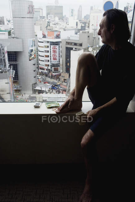 Hombre sentado en la repisa de la ventana mirando a la vista - foto de stock