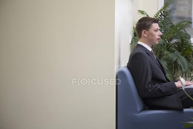 Un joven hombre de negocios sentado en una recepción de oficina - foto de stock