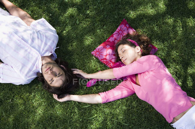 Una joven pareja yaciendo en la hierba juntos - foto de stock