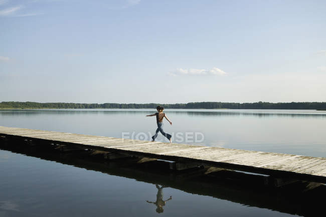 Mujer vista lateral corriendo en embarcadero en el lago tranquilo - foto de stock