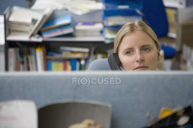 Una mujer usando un teléfono en un cubículo de oficina - foto de stock