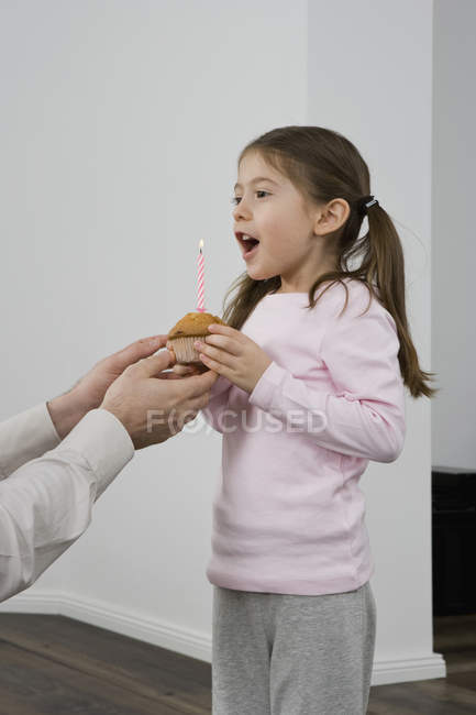 Ein junges Mädchen erhält einen Muffin mit einer Geburtstagskerze darin — Stockfoto