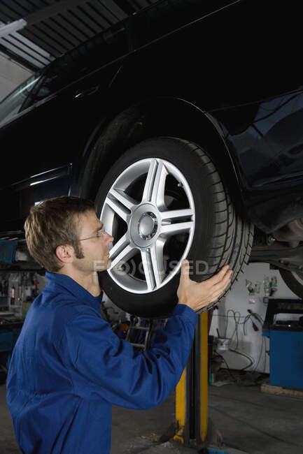 Un mecánico que fija la rueda de un coche en un garaje de reparación - foto de stock