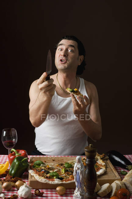 Hombre italiano estereotipado comiendo pizza y sosteniendo un cuchillo agresivamente - foto de stock