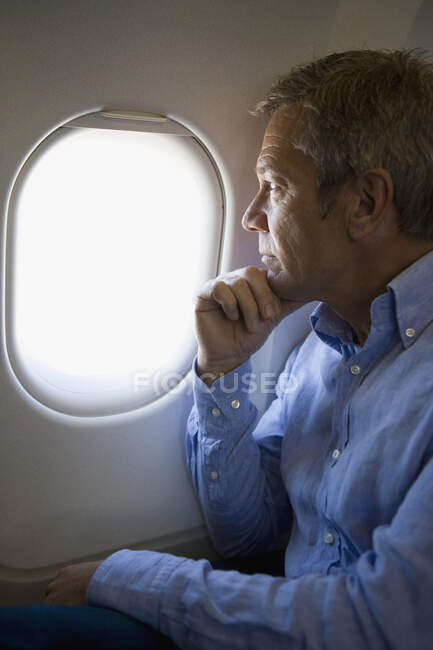 Un pasajero en un avión mirando por la ventana - foto de stock