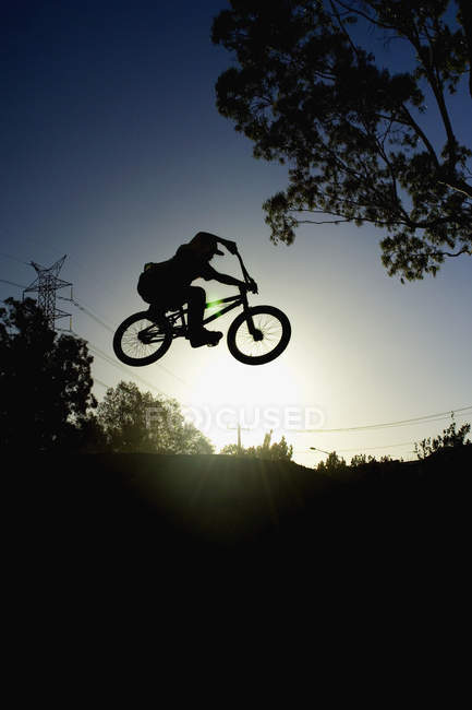 Silueta de la persona haciendo un truco en una bicicleta BMX - foto de stock