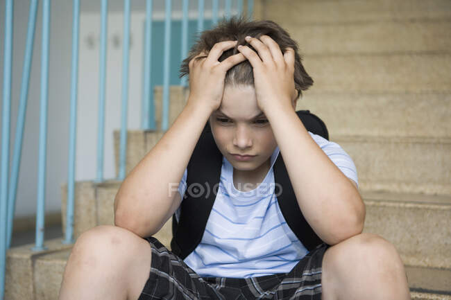 Um menino pré-adolescente preocupado sentado nas escadas de uma escola — Fotografia de Stock
