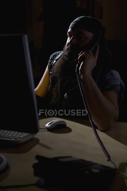 A biker sitting in a darkened office on the phone — Stock Photo
