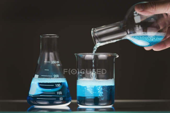 Cultivo mano masculina verter líquido azul en vaso de precipitados - foto de stock