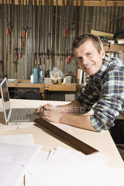 Portrait de menuisier souriant à l'aide d'un ordinateur portable en atelier — Photo de stock