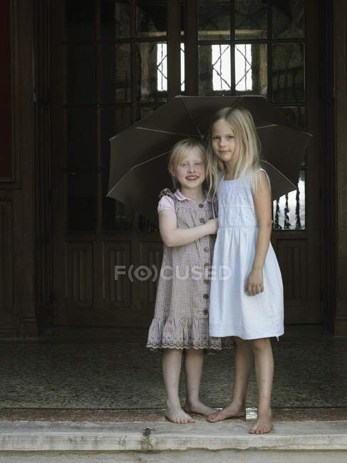 Dos chicas paradas debajo de un paraguas - foto de stock