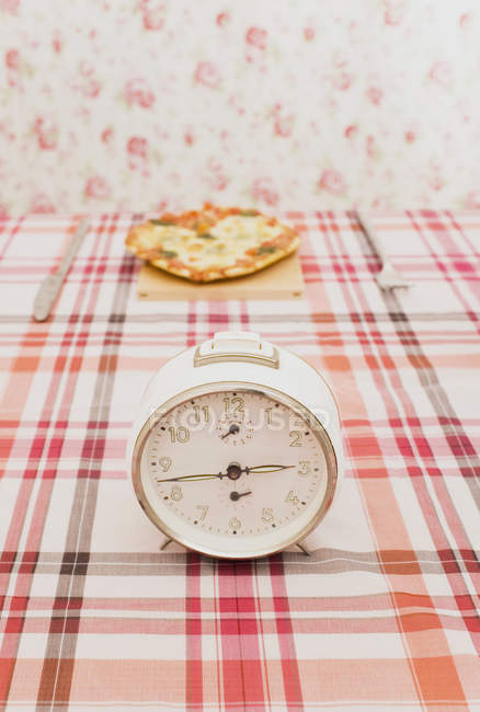 Old fashioned clock on table with a pizza — Stock Photo