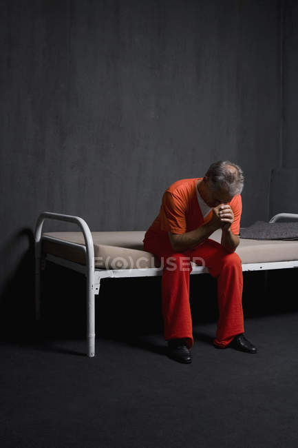 Печальный заключенный сидит на кровати в камере — стоковое фото