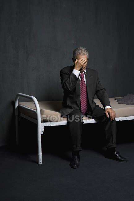 Triste hombre de negocios sentado en una cama en la celda de la prisión - foto de stock