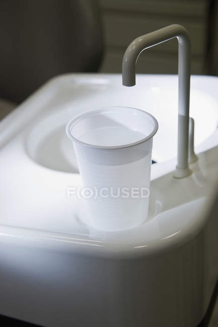 Plastic cup of water at the edge of dental cuspidor — Stock Photo
