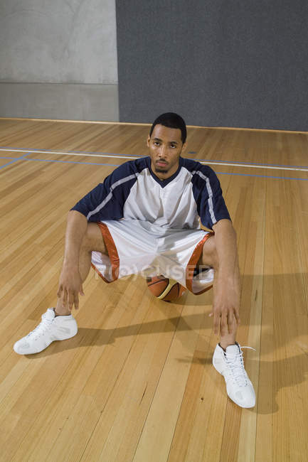 Un giovane uomo che sembra serio seduto su un pallone da basket — Foto stock
