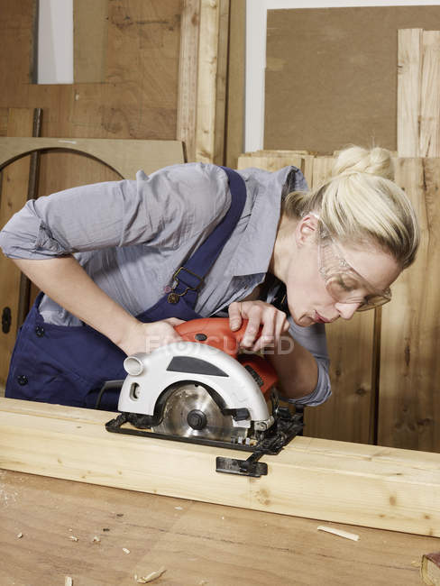 Young woman sawing wood in workshop — Stock Photo