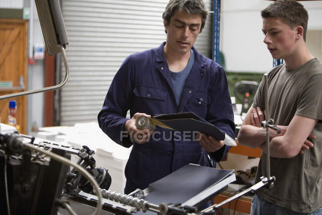 Un hombre entrenando a un joven en una imprenta - foto de stock