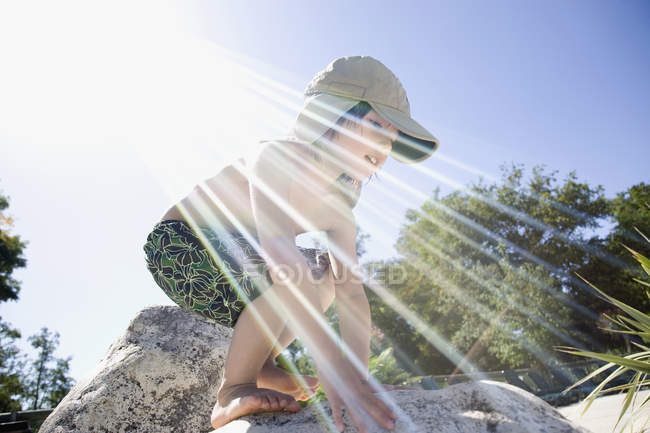 Sun rays shining around a young boy climbing on rocks — Stock Photo