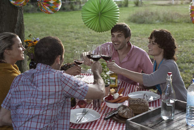 Cuatro personas en una cena levantando sus copas de vino en un brindis - foto de stock