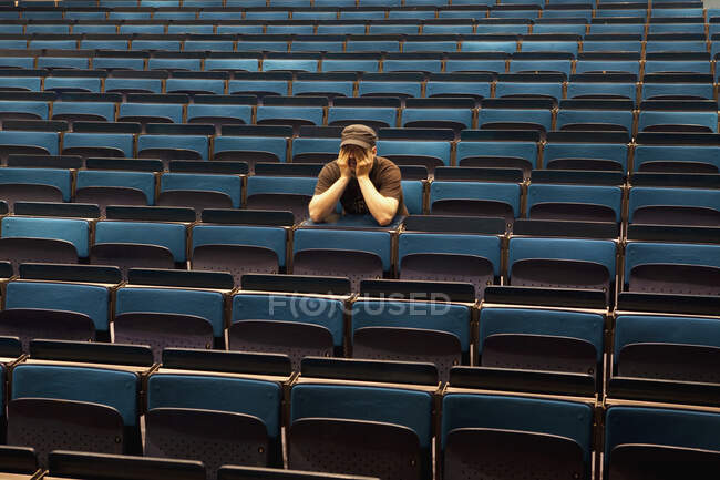 Un hombre sentado en un auditorio, manos cubriendo los ojos - foto de stock