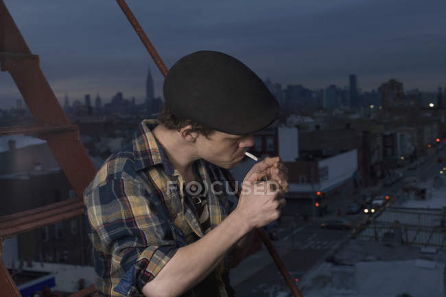 Young man standing on a fire escape and lighting a cigarette — Stock Photo