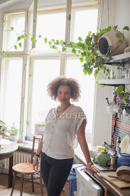 Porträt einer jungen Frau, die zu Hause am Küchentisch gegen Fenster steht — Stockfoto