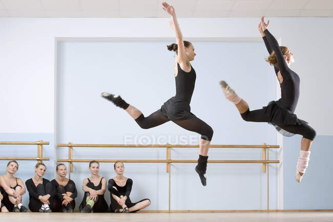 Dos bailarinas saltando por el aire mientras otras miran - foto de stock
