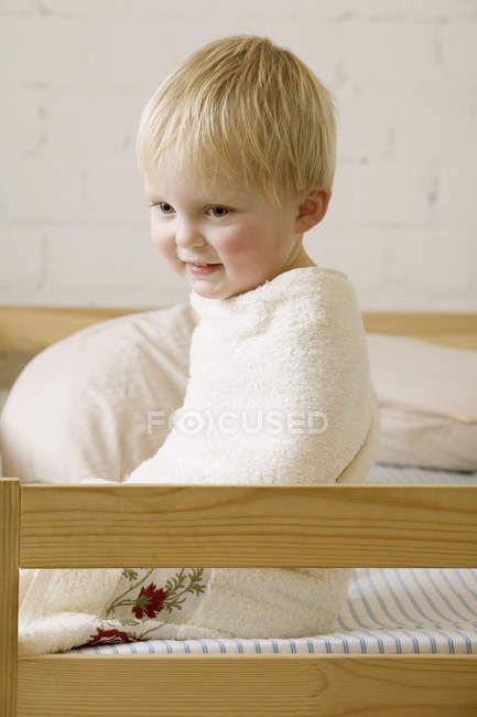 Un Bebe Garcon Heureux Enveloppe Dans Une Serviette Assise Sur Un Lit Enfant Mode De Vie Stock Photo