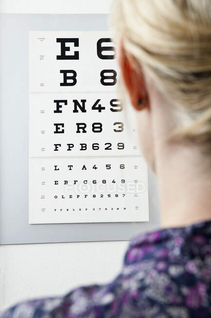 A woman reading an eye chart, over the shoulder view — Stock Photo